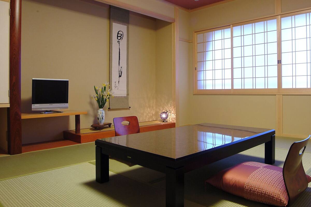 Una habitación japonesa tradicional con suelo de tatami, una mesa baja, un televisor y un celosía japonesa.