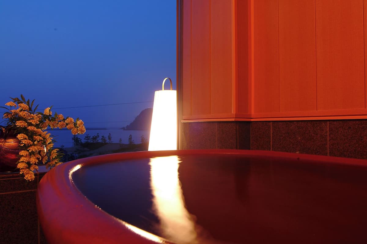 Una bañera roja con luz blanca, pared de azulejos y vista al océano.