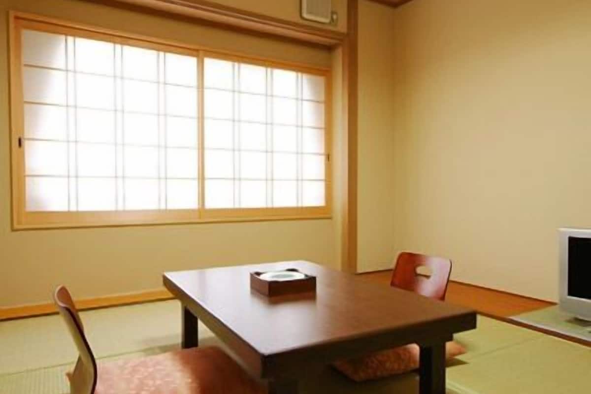 Una habitación japonesa tradicional con suelo de tatami, una mesa baja, una silla y un televisor.