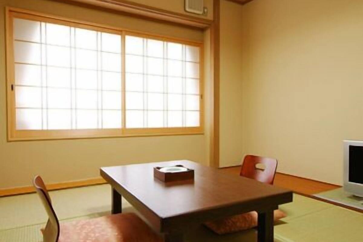 A traditional Japanese room with tatami flooring, a low table, a chair, and a television.