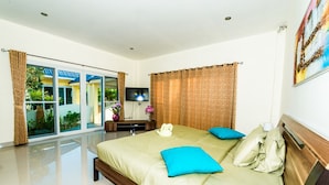 A modern hotel room with a large bed, a flat-screen TV, and a sliding glass door leading to a balcony. - Platinum 3 bedrooms villa pool garden (Rawai)