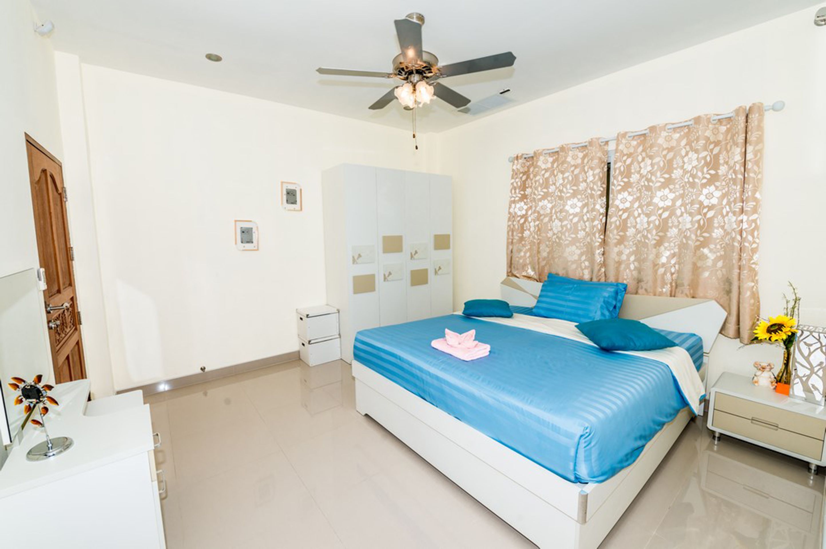 A bedroom with a bed, a ceiling fan, a nightstand, a wardrobe, and a window with curtains.