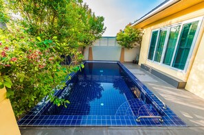 A rectangular swimming pool with blue tiles, surrounded by greenery and a building with large windows. - Platinum 3 bedrooms villa pool garden (Rawai)
