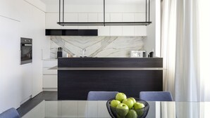 A modern kitchen with a marble backsplash, black cabinetry, and a glass dining table with a bowl of green apples. - Botanik Apartment Hotel (Surry Hills)