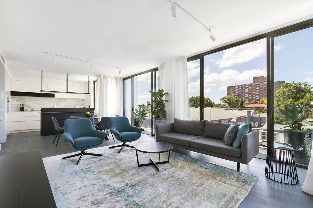 A modern living room with a sofa, two armchairs, a coffee table, and a large window offering a city view.