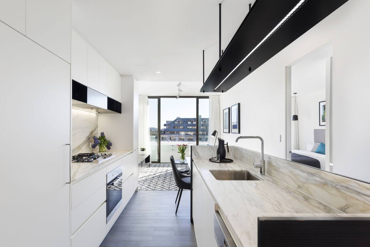 A modern kitchen with white cabinetry, a marble countertop, and a view of the city through large windows.