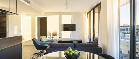 A modern living room with a glass table, a sofa, and a TV on the wall.