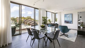 A modern dining area with a glass table, grey chairs, and a large potted plant. - Botanik Apartment Hotel (Surry Hills)