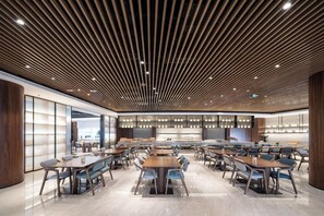Un'area ristorazione moderna con diversi tavoli e sedie, soffitto in legno a listelli e un'atmosfera luminosa e accogliente.