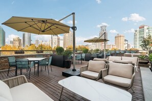Un'area salotto all'aperto con tavoli e sedie, ombrelloni e una vista sullo skyline della città.