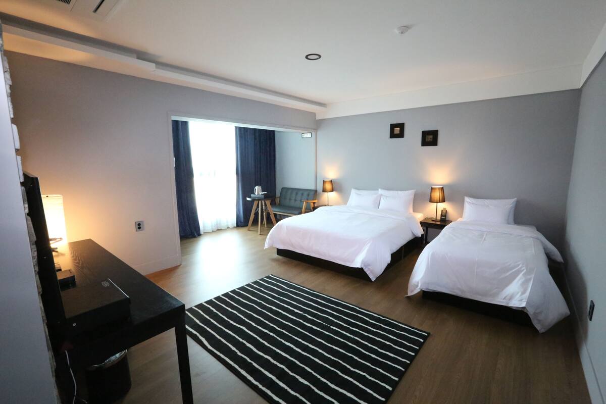 A hotel room with two beds, a desk, a chair, and a view of the outside.