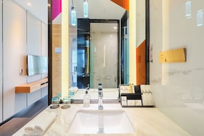 Un baño moderno con un lavamanos grande, un espejo y un televisor montado en la pared.