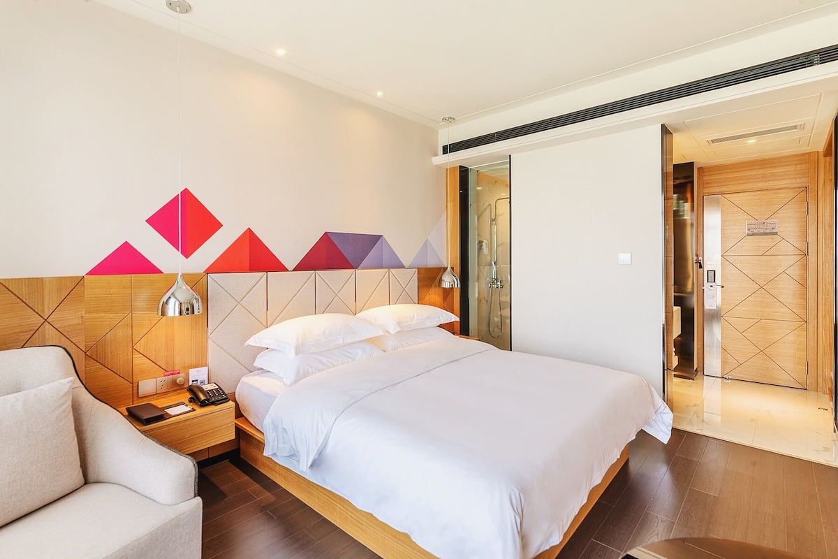 Une chambre d’hôtel moderne avec un grand lit, une table de chevet avec une lampe, une chaise et un espace douche.