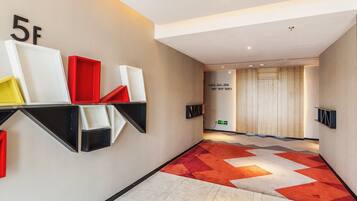A hallway with a geometric patterned carpet, a wall-mounted shelf with variously colored objects, and a door with directional signage.
