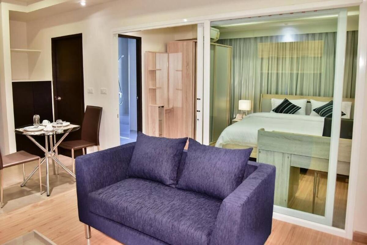 Una habitación de hotel moderna con sofá, cama, zona de comedor y puerta corrediza al balcón.