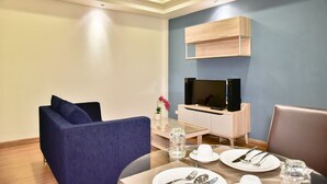 A modern living room with a sofa, dining table set for two, a TV on a wooden stand, and a small potted plant. - The Kaze 34 Hotel and Serviced Residence (Bangkok)