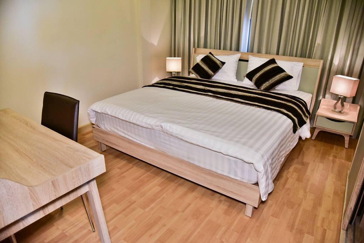 Una habitación de hotel con cama, mesitas de noche, una silla y suelo de madera.