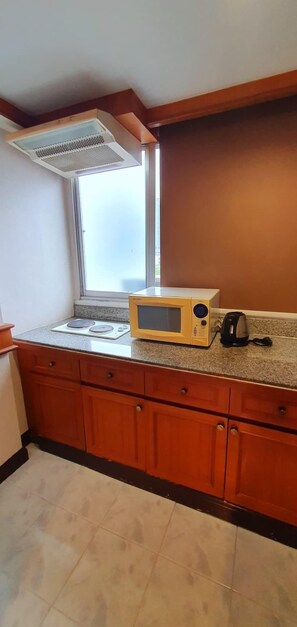 A kitchen with wooden cabinets, a microwave, a kettle, and a window with blinds. - The Kaze 34 Hotel and Serviced Residence (Bangkok)