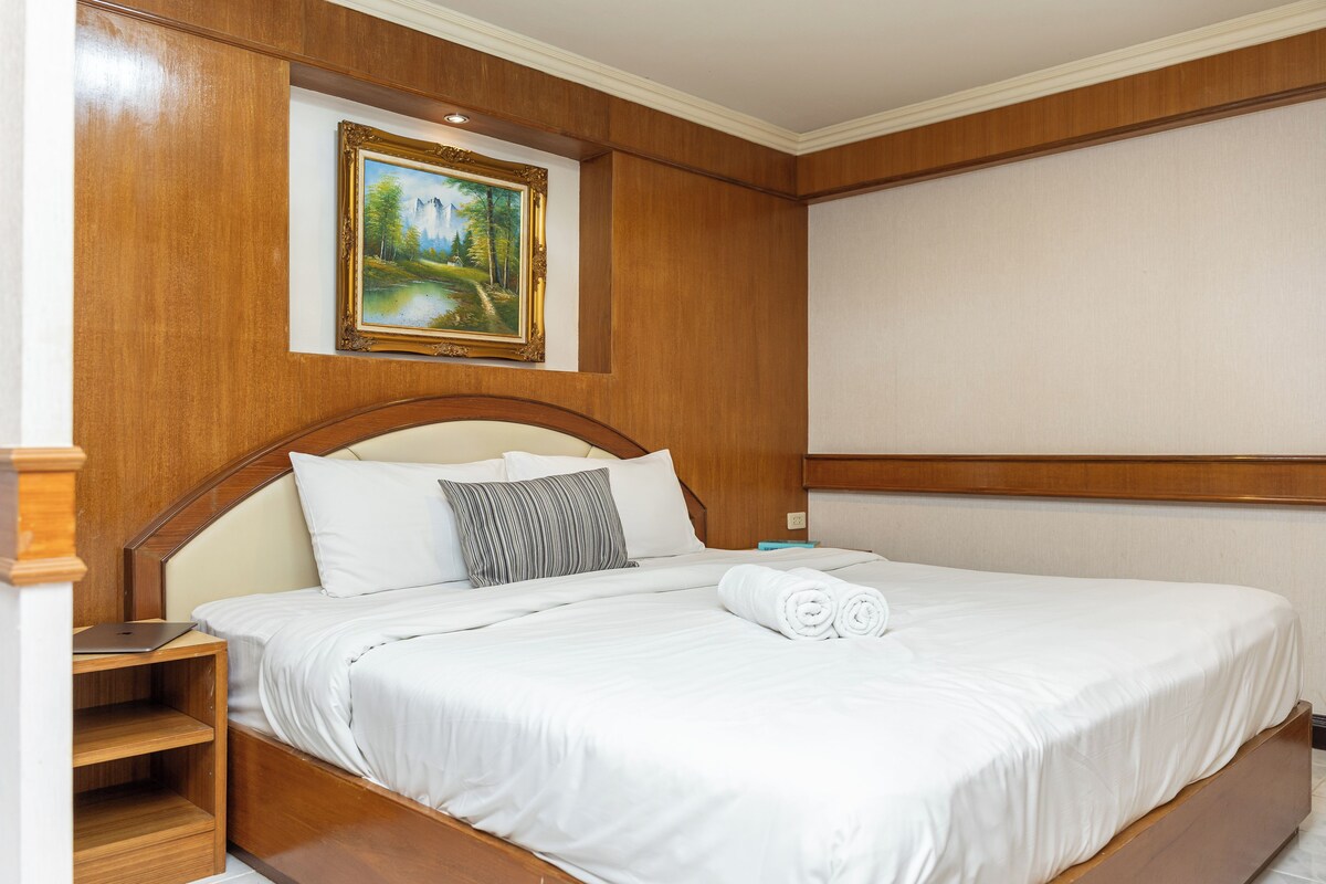 A hotel room with a bed, a nightstand, a laptop, and a painting on the wall.