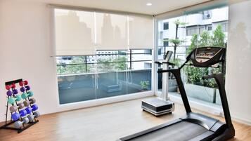 A modern gym with a treadmill, a weight rack, and a large window offering a city view.