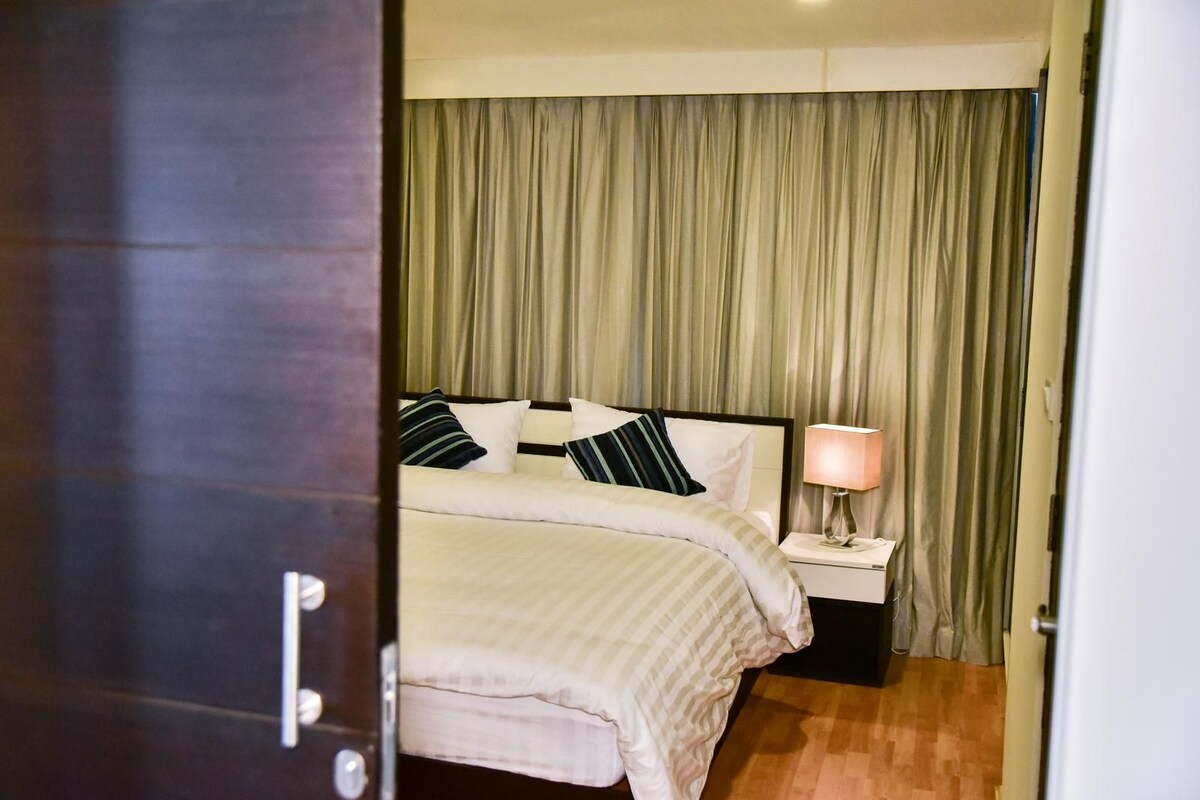 Una habitación de hotel con una cama, una mesita de noche, una lámpara y una cortina.