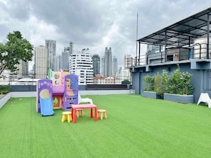Una azotea con césped artificial, juegos infantiles y vistas a un horizonte urbano.