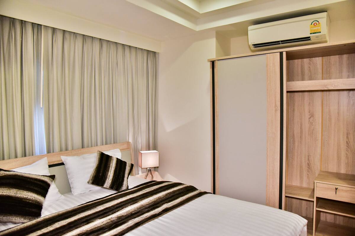 Una habitación de hotel con cama, mesita de noche, lámpara, armario y aire acondicionado.
