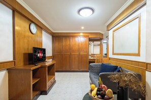 A living room with wooden cabinets, a television, a sofa, and a fruit basket.