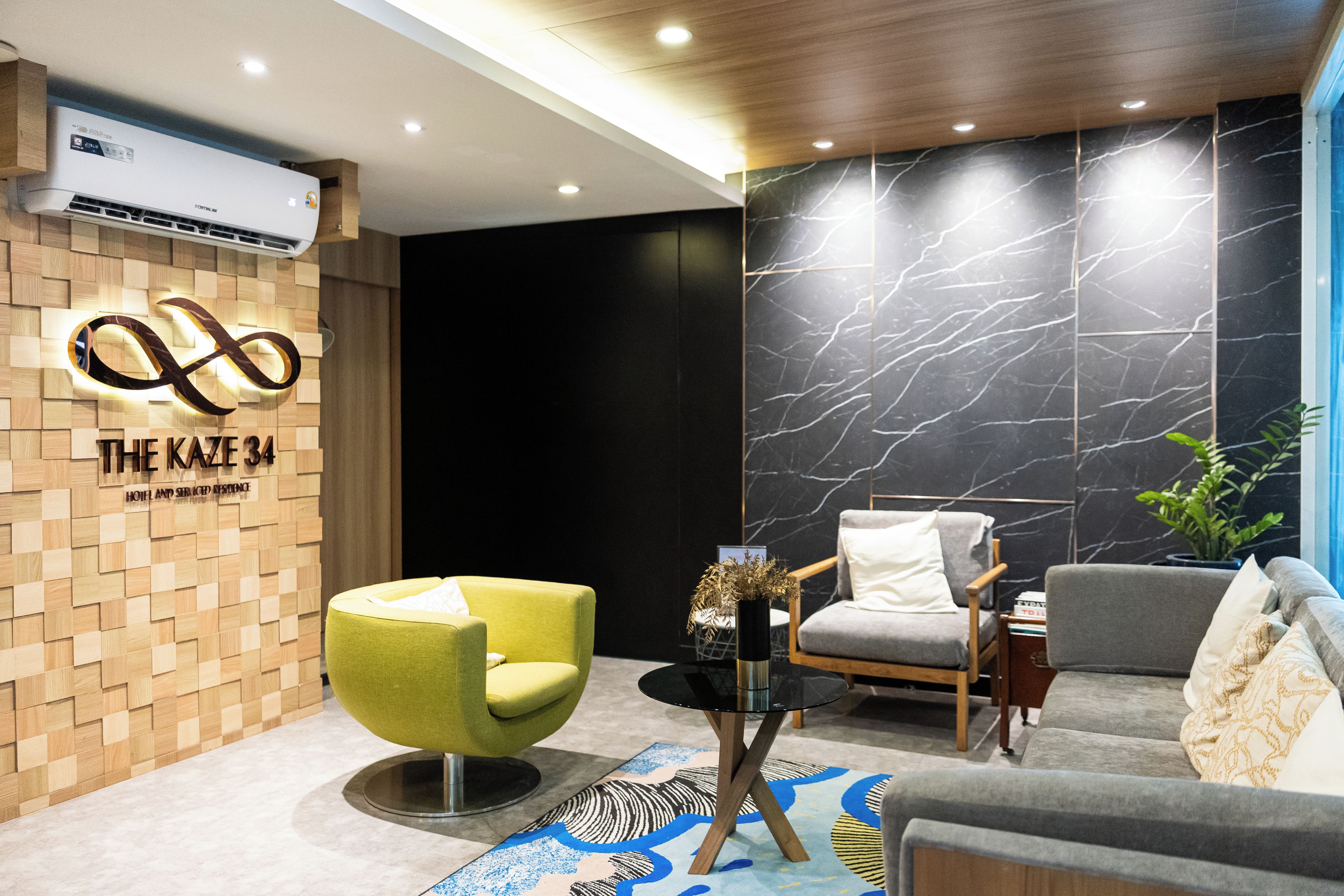 A modern hotel lobby with a wooden wall, a marble wall, and a seating area with a green chair and two sofas.