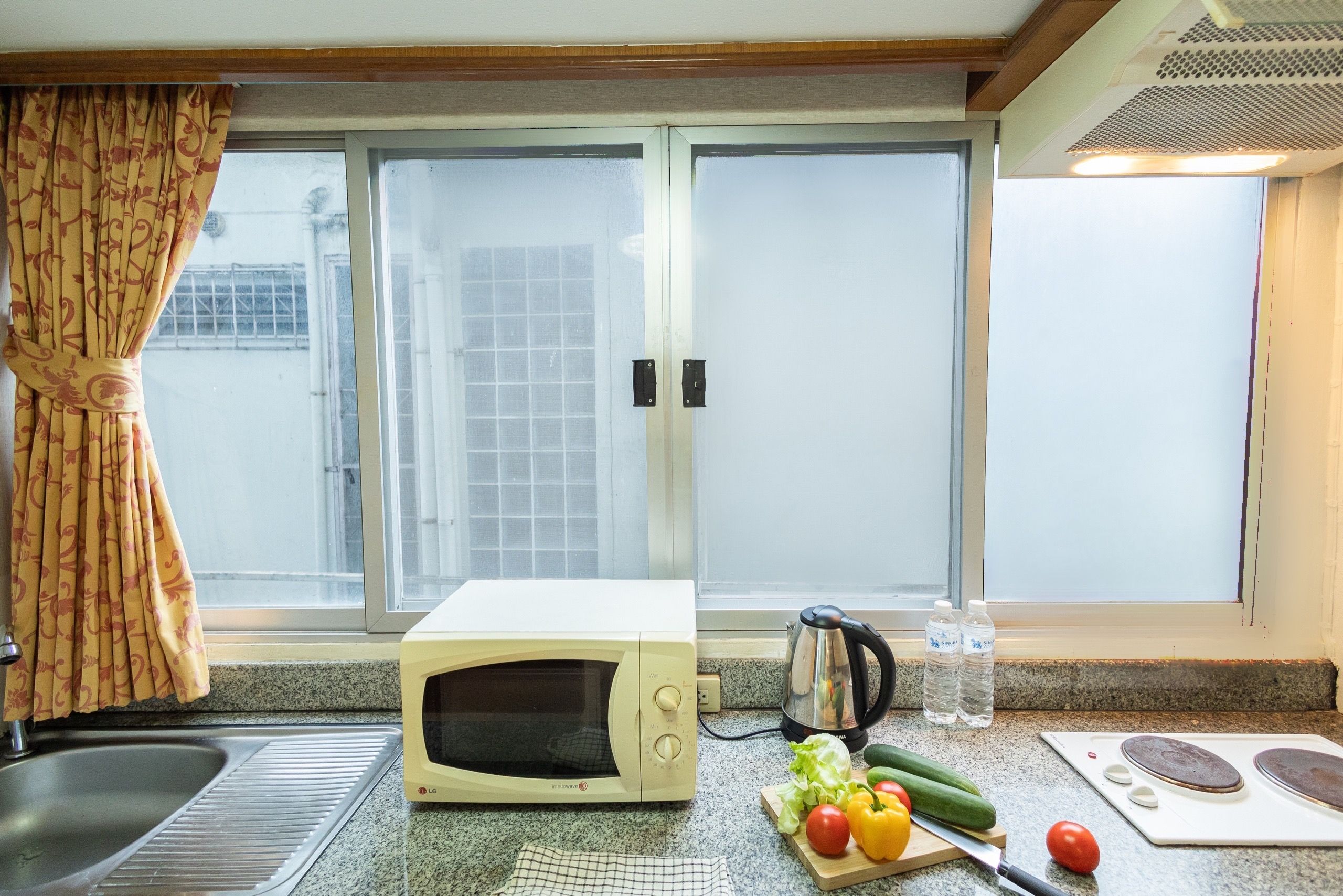 A kitchen with a microwave, kettle, and fresh vegetables on the counter.