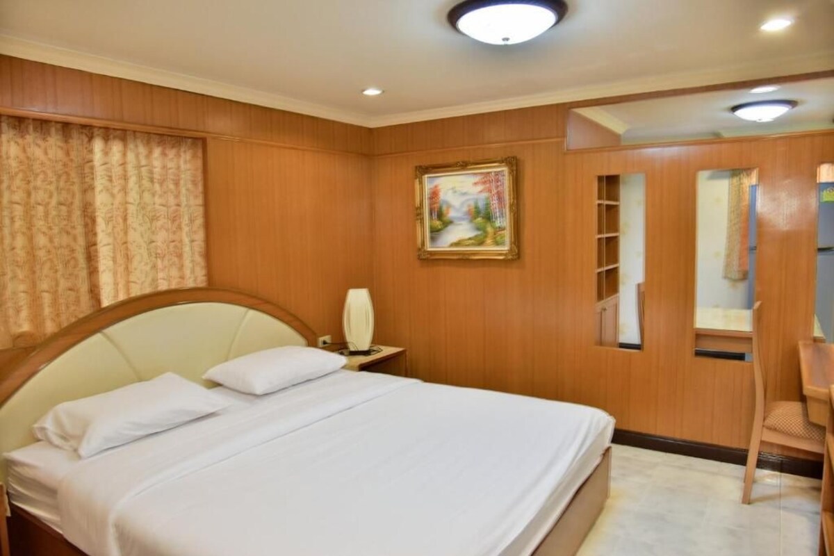 A hotel room with a bed, a nightstand, a painting, a mirror, and a wardrobe.