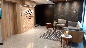 A modern reception area with a wooden wall, a marble-patterned wall, and a grey sofa. - The Kaze 34 Hotel and Serviced Residence (Bangkok)