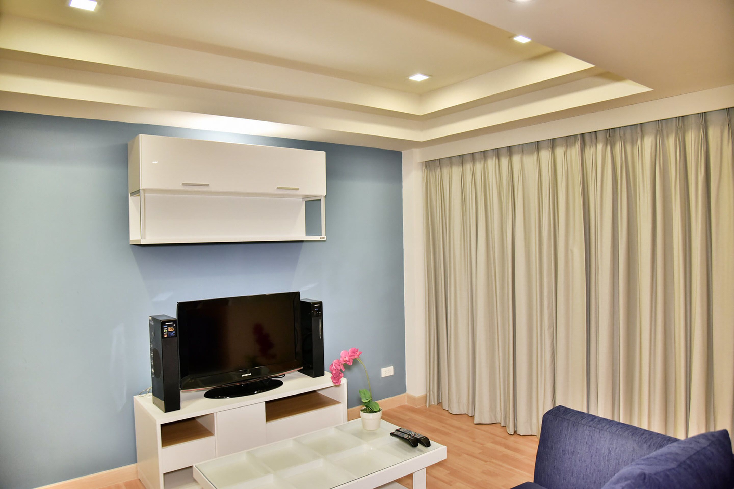 Un salon moderne avec un téléviseur à écran plat, un meuble de rangement blanc et une télécommande posée sur une table basse en verre.