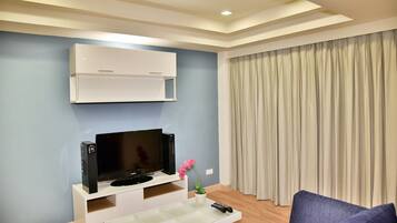 A modern living room with a flat-screen TV, white entertainment unit, and a remote control on a glass coffee table.