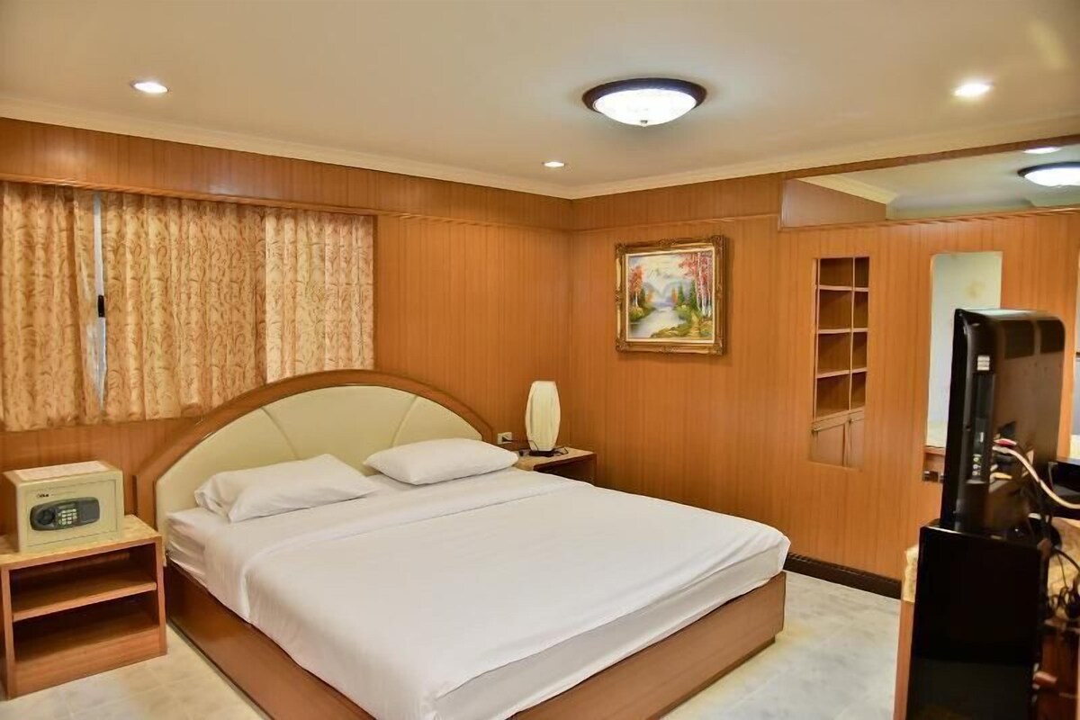 A hotel room with a bed, bedside table, lamp, painting, and television.