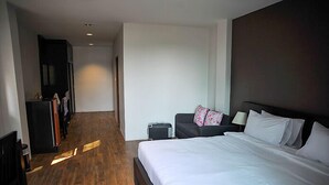 Habitación de hotel con una cama grande, un escritorio, una silla, un armario y una pequeña mesa con lámpara.