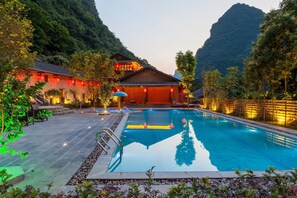 Una piscina con cubierta de madera, rodeada de árboles y con una montaña de fondo.