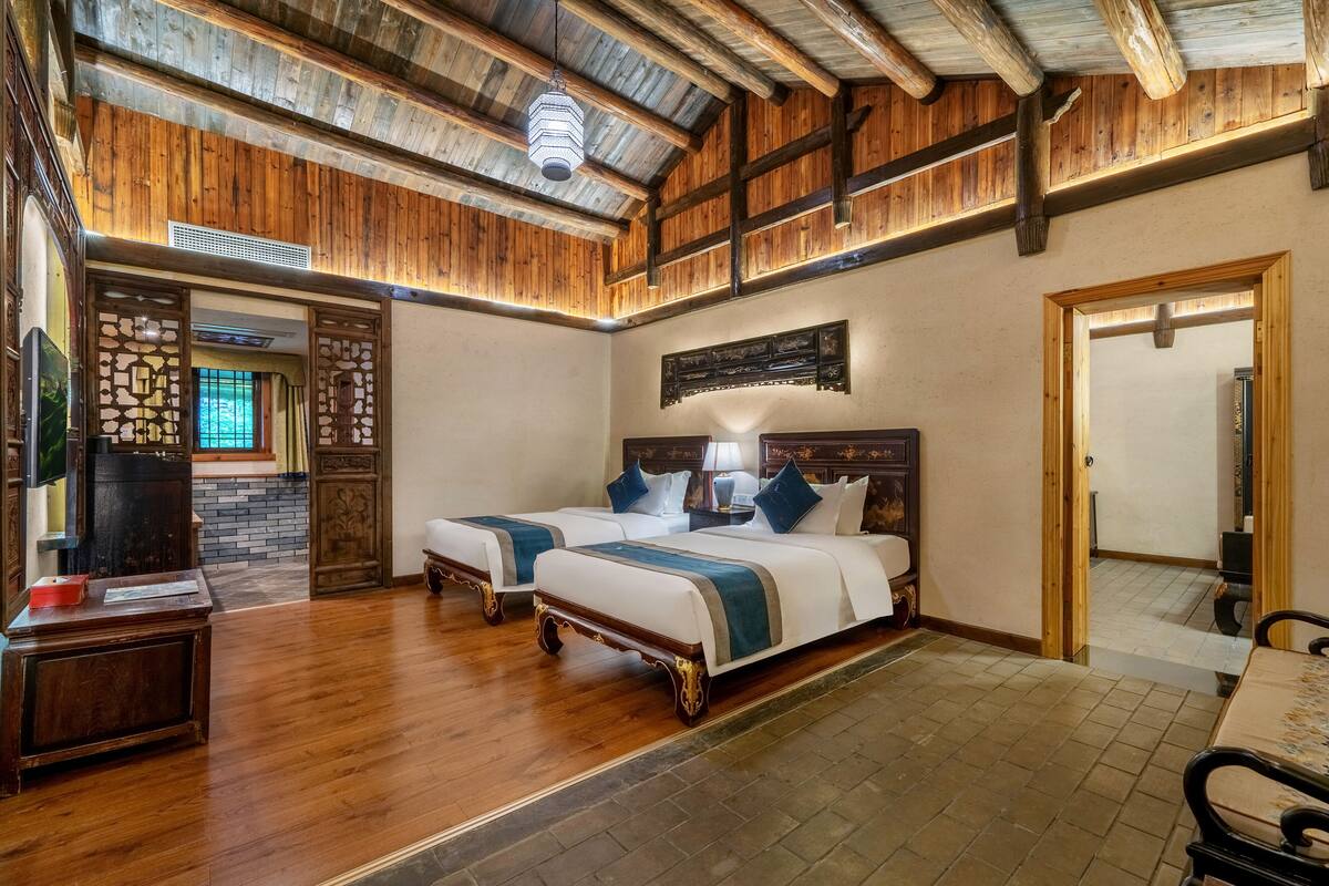 A hotel room with two beds, wooden flooring, a wooden ceiling, and a brick wall.