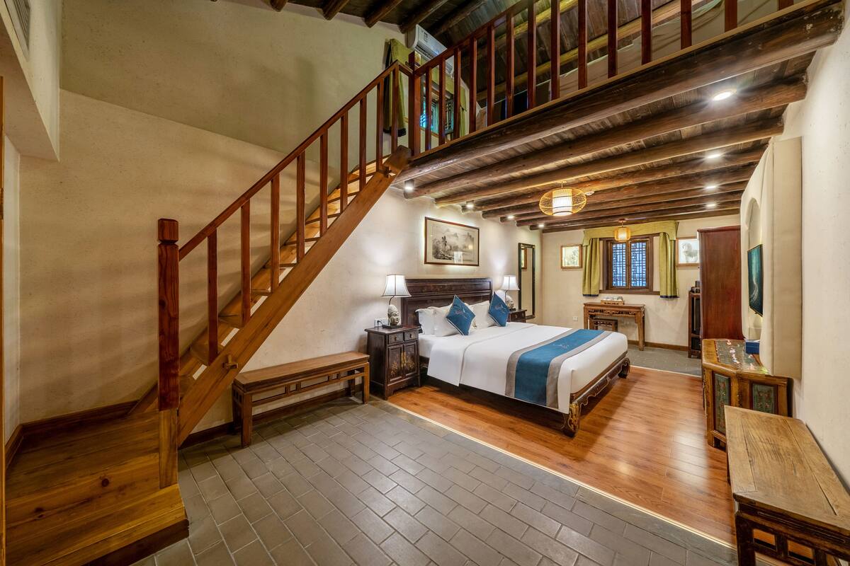 A bedroom with a wooden staircase, a large bed, a nightstand, and a wooden bench.