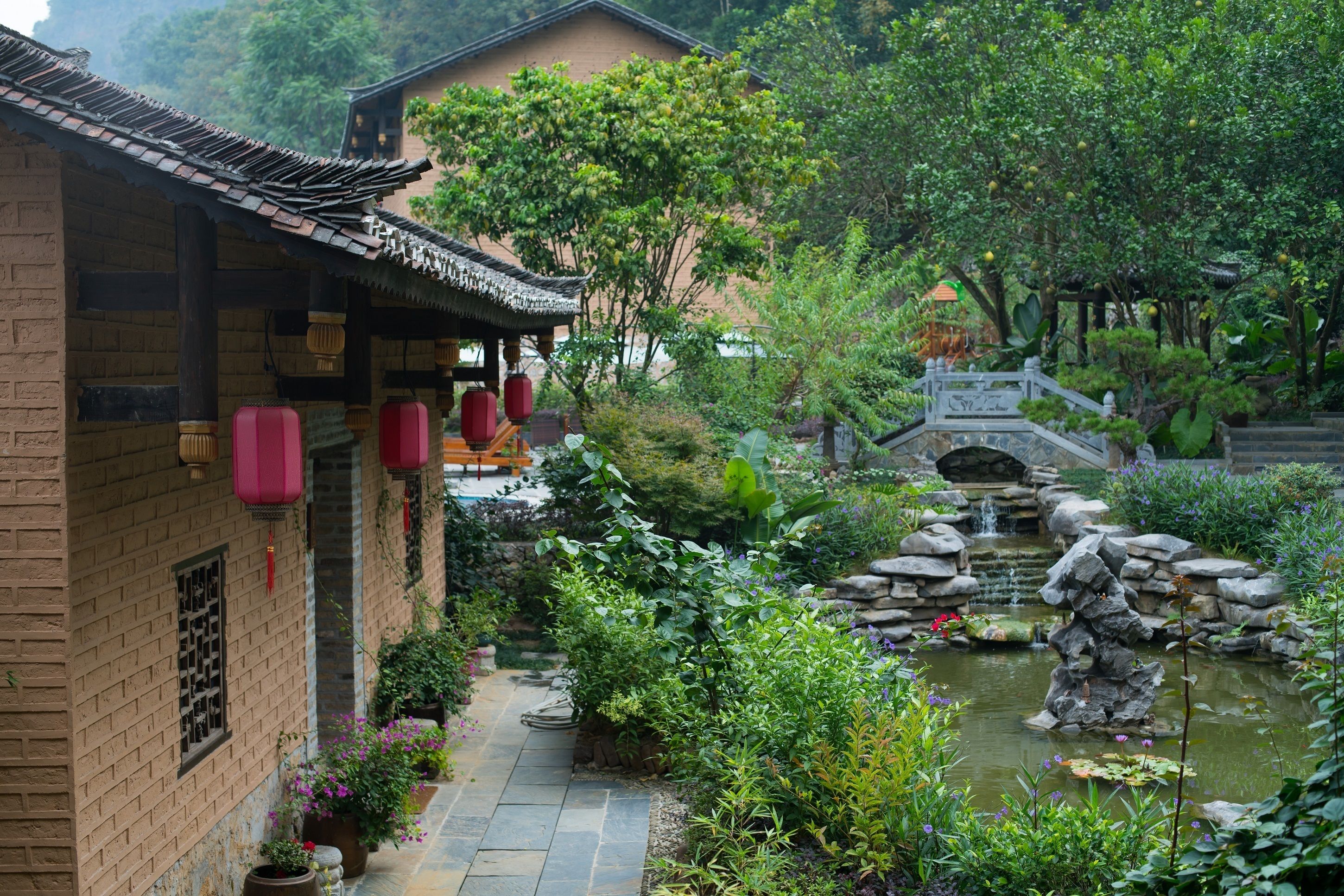 A traditional courtyard with a stone pathway, a small bridge, and a pond with rocks and plants.