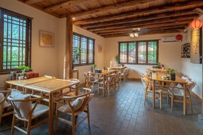 Un interior de madera tradicional con varias mesas y sillas de comedor, ventanas amplias con marcos de madera y un techo rústico.