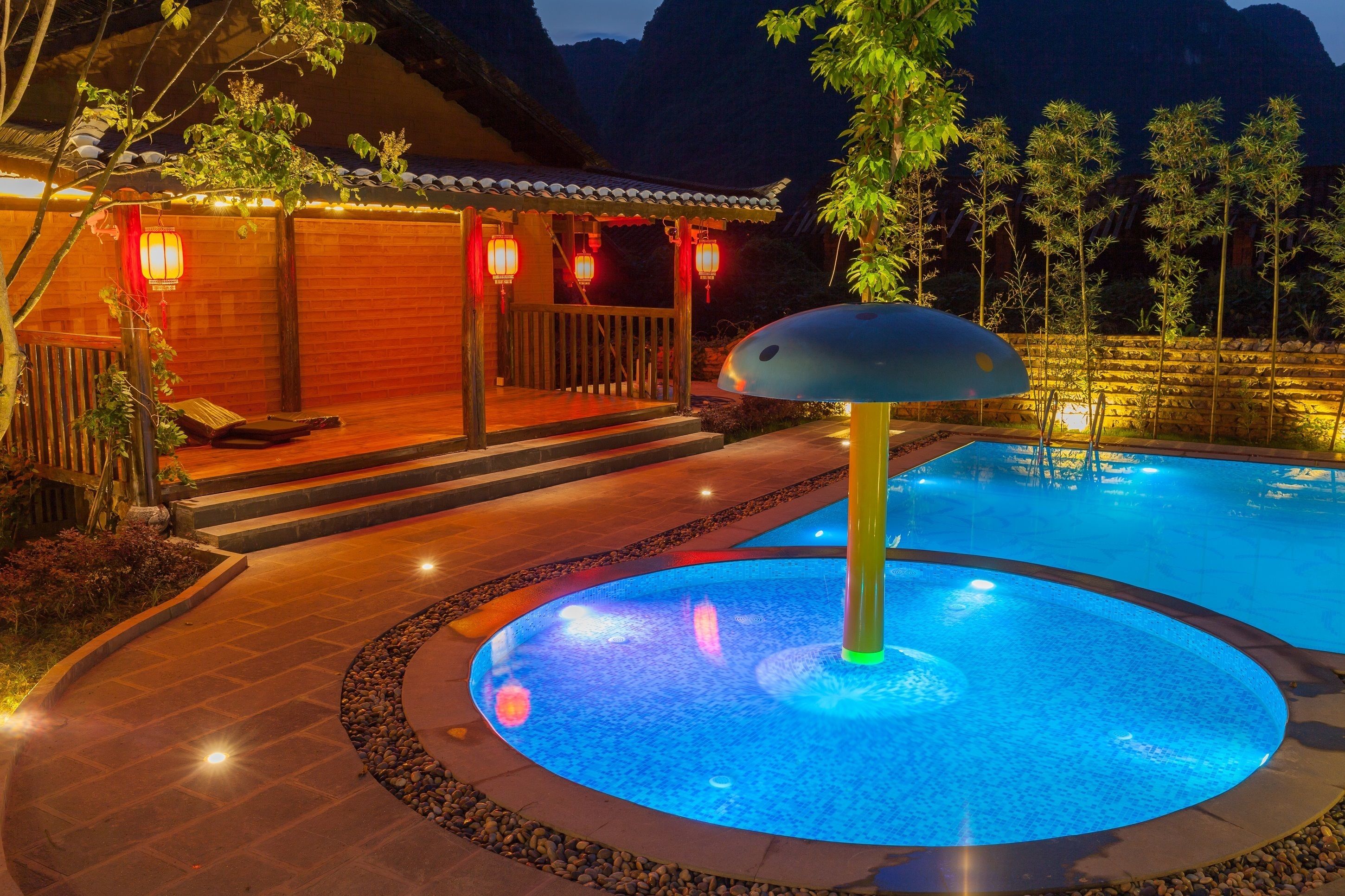 Uma piscina com uma fonte central, rodeada por um deck de madeira e um caminho de pedra.