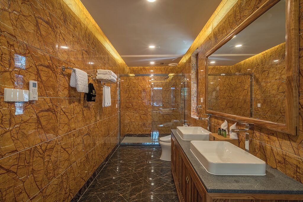 A modern bathroom with marble walls, a large mirror, two sinks, and a shower area.