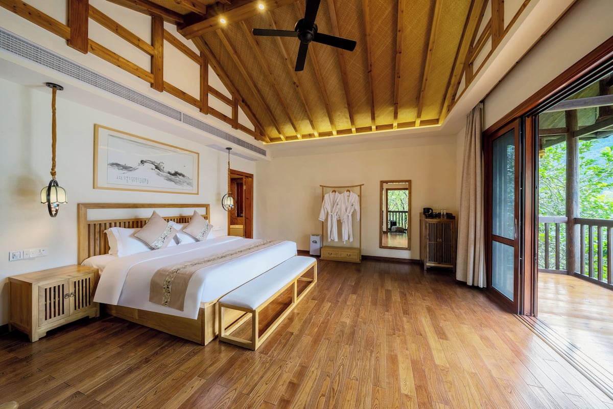 A spacious bedroom with a large bed, wooden flooring, a ceiling fan, and a view through a sliding glass door.