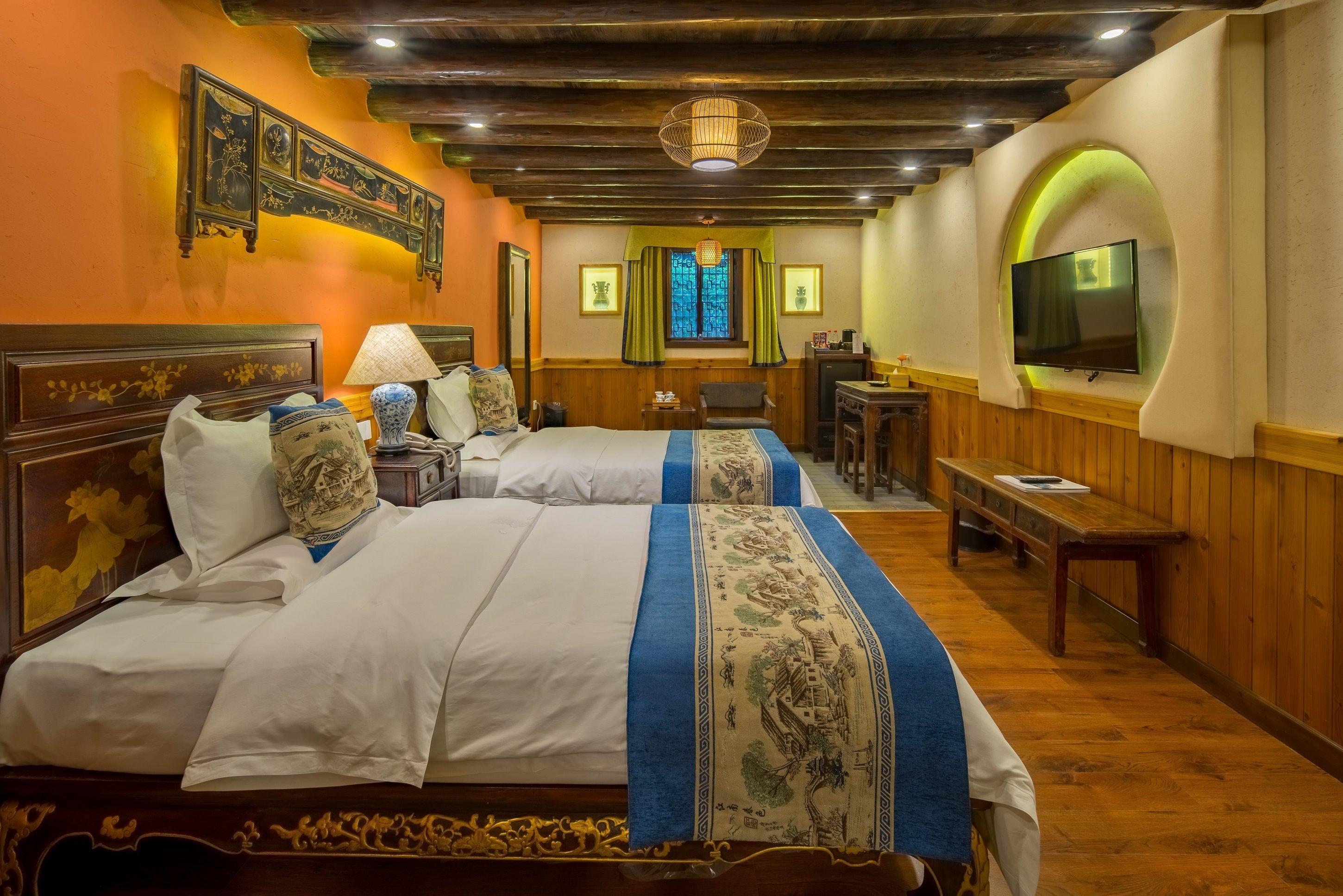 A hotel room with two beds, wooden flooring, a television mounted on the wall, and a traditional Chinese decorative wall piece.