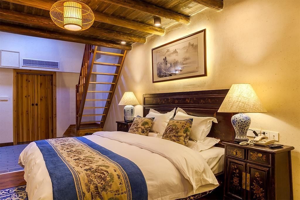 A bedroom with a wooden bed, two bedside lamps, a nightstand, a framed picture on the wall, and a wooden ladder leading to an upper level.