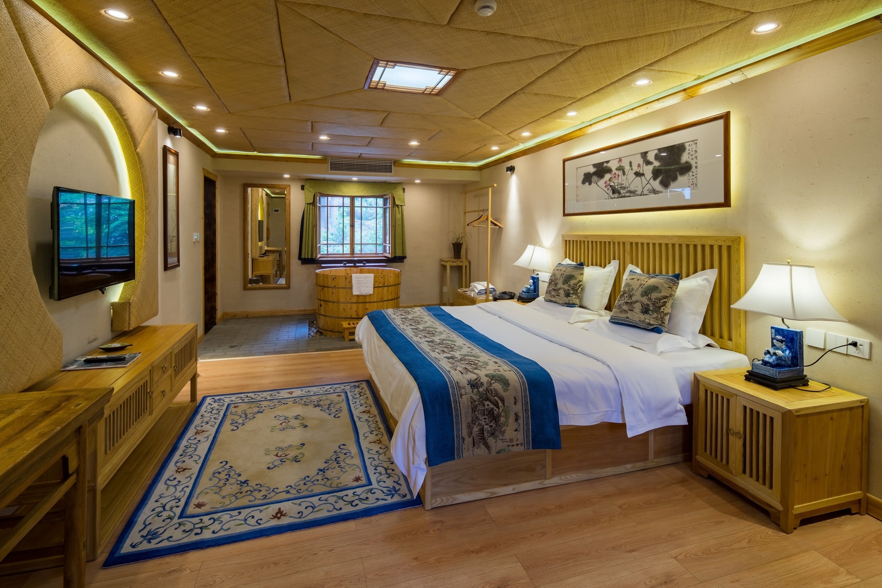 Quarto de hotel com cama, mesas de cabeceira, televisão, armário de madeira, escrivaninha, cadeira, tapete e janela com cortinas.