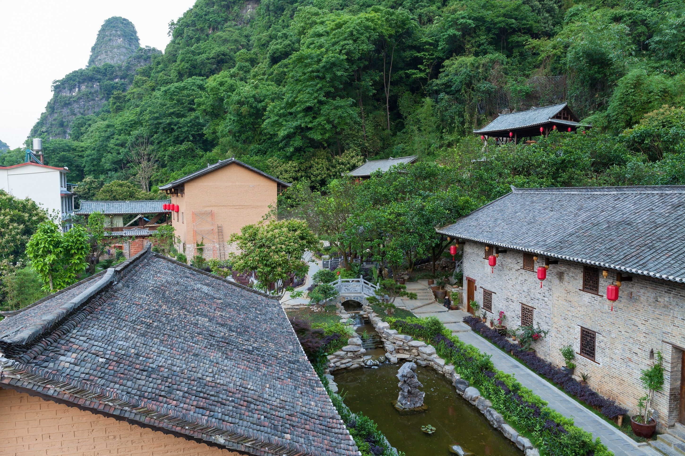 A traditional Chinese village with stone buildings, a small bridge, and a pond.