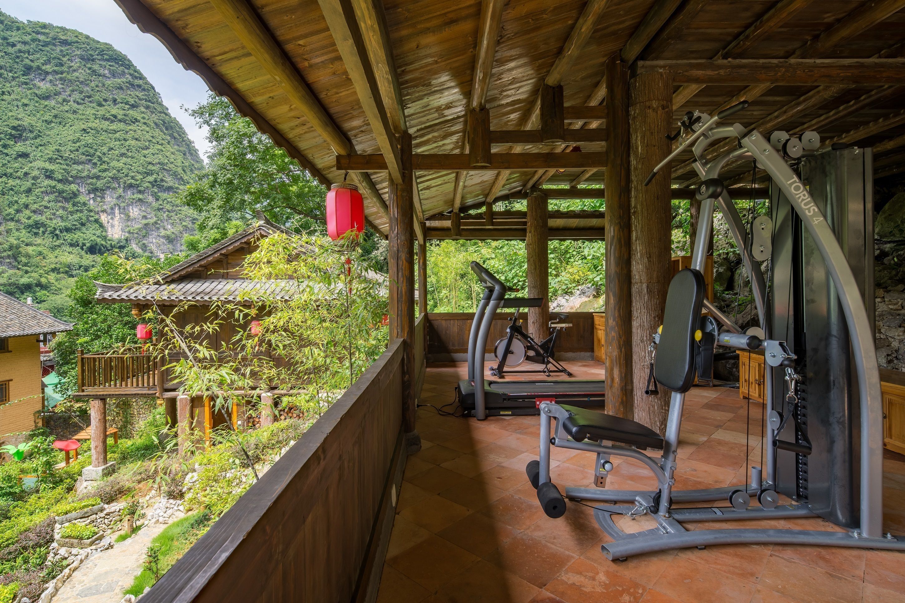Un espace de remise en forme extérieur abrité, équipé de matériel d’exercice, offrant une vue sur un paysage montagneux et des bâtiments traditionnels.