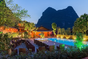 A poolside area with wicker chairs, a building with traditional architecture, and a mountainous backdrop. - Yangshuo Ancient Garden Boutique Hotel (Guilin)